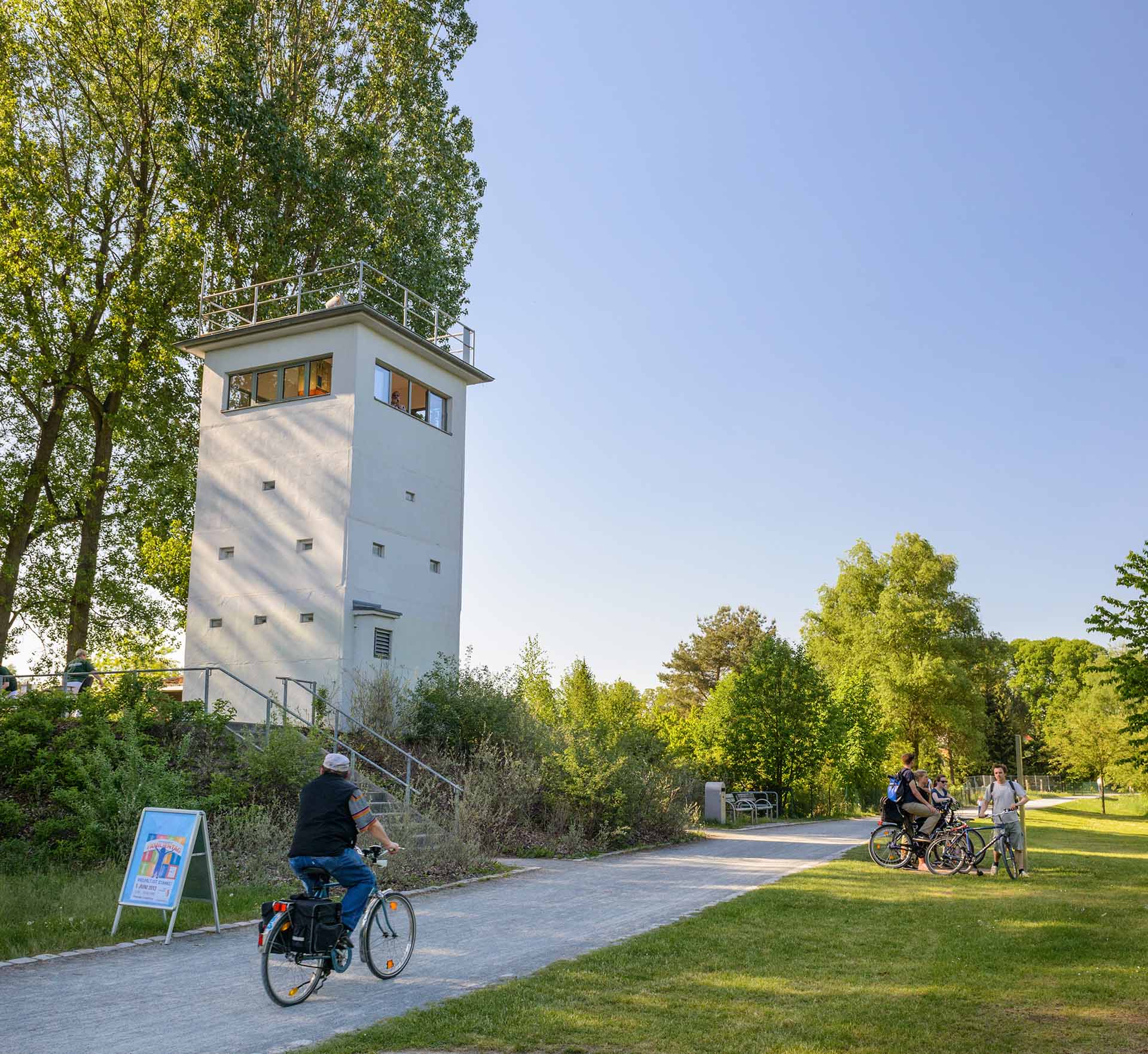 Person auf Fahrrad fährt an einem sonnigen Tag am Grenzturm vorbei