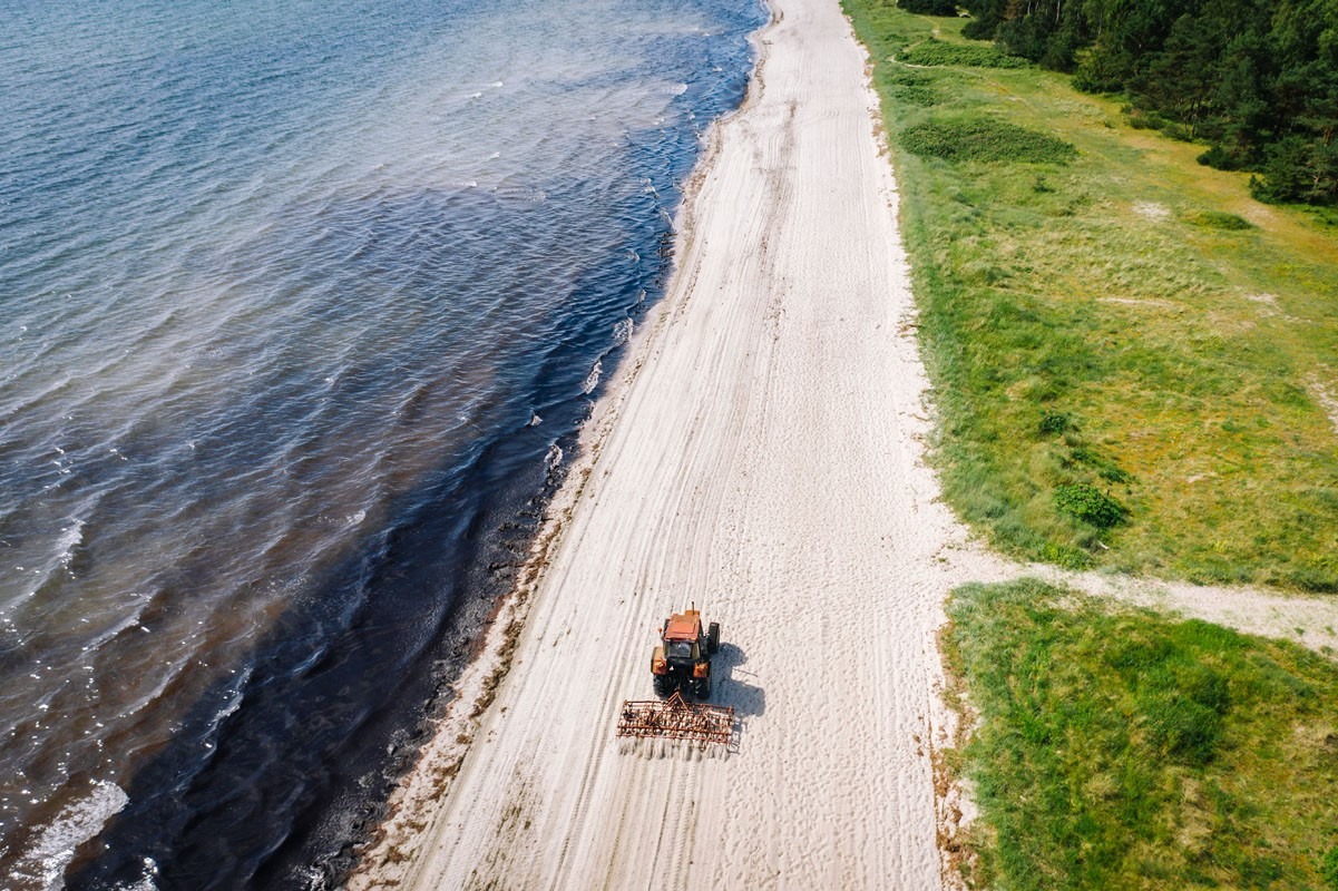 Luftbild vom Badestrand am Præstøfjord mit einem fahrenden Traktor im Sand